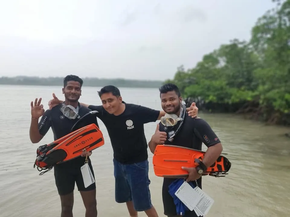 Hardik with two freediving candidates holding long fins beside mangroves after a field session