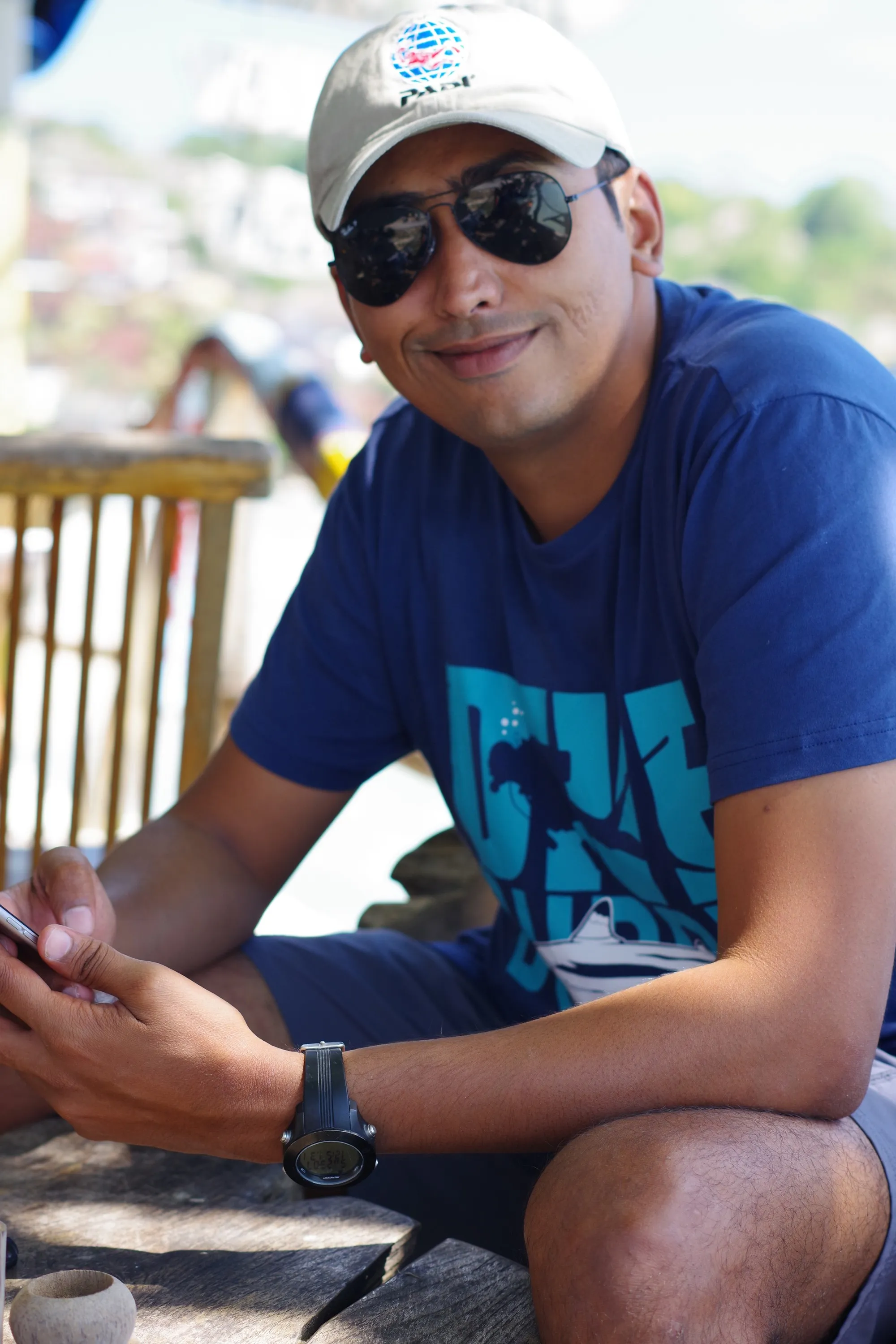 Portrait of Hardik Datanwala in a PADI cap and dive T-shirt, seated at the coast
