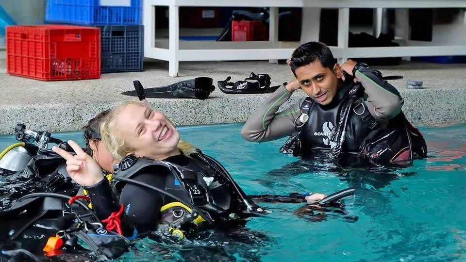 Hardik conducting confined-water training in a pool, gearing up beside a smiling student in full scuba equipment